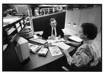 2003-732 Een medewerker van de Ondernemerswinkel staat een klant te woord aan het bureau in zijn kantoor in de hal van ...