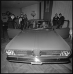 10530-1 Mannen bekijken een Plymouth-Valiant auto in de expositiezaal.