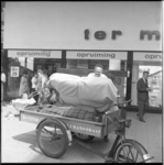 8173-2 Man plaatst een matras op zijn bakfiets/fietscarrier tijdens de uitverkoop en opruiming van warenhuis Ter Meulen ...