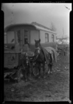 THO-109 Een kind met sjaal en muts staat met een paard bij een woonwagen in een woonwagenkamp aan de Middeldijk in ...