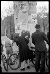 1980-5597 Mensen lezen Nederlandse proclamaties en 'bekendmakingen' op een aanplakzuil aan de Bergse Dorpsstraat in ...