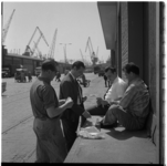 21809 Pauzerende arbeiders bezig met een potje kaarten in de Radiostraat bij de Merwehaven. Op de achtergrond meerdere ...
