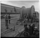 36735 Mannen rollen een kabel af van een grote haspel bij werkzaamheden aan een zinker bij het Calandkanaal.