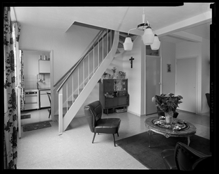 L-10064 Woonkamer met trap naar boven. Op de achtergrond de keuken. In de kamer staan een stoel, een salontafel, een ...