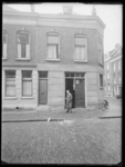 L-1581 Een man staat bij een geopende deur van een woning in de Koepelstraat. Tegen de gevel staat een fiets.