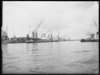 L-1909 Met kranen worden zeeschepen gelost in de Merwehaven. Binnenvaartschepen liggen langszij. Links aan de kade ...