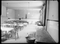 L-1939 Eetzaal met gedekte tafels. Links tegen de muur staan genummerde lockers, rechts op de voorgrond een wastobbe. ...