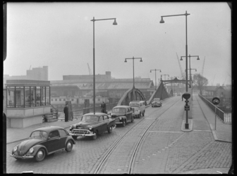 L-438 Personenauto's rijden door de Stieltjesstraat over de Spoorweghavenbrug over de Spoorweghaven. Links van de brug ...