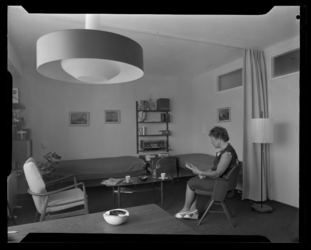 L-7051 Interieur van een woning aan de Catullusweg. Een zittende vrouw die een tijdschrift leest.