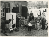 1977-3975 Enkele mensen zijn bezig met het schoonmaken van bakkerijmachines, die als gevolg van watersnoodramp smerig ...