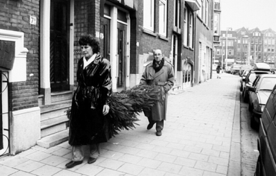 2000-1054-3 Een man en een vrouw dragen een kerstboom naar huis in de Claes de Vrieselaan. Op de achtergrond: het ...
