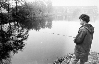 2001-959 Een man staat te vissen in een plas bij het Katershofpad in Overschie. Op de achtergrond huizen langs de Wouwerlaan