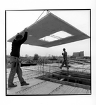 2003-745 1 bouwvakker plaatst een betonnen tussenverdieping op een gebouw in aanbouw, terwijl een andere bouwvakker ...
