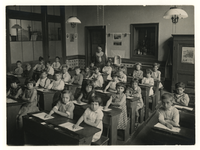 1975-383 Onderwijzeres M. van Loon met haar leerlingen in een klas van de school in de omgeving van de Crooswijksesingel (?).