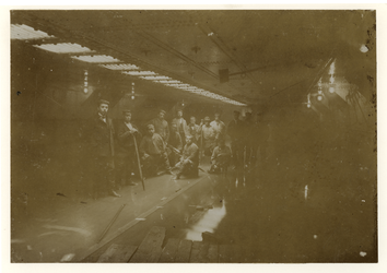 1976-213 Een groep arbeiders in een tunnelstuk van geklonken metaal, poserend voor een fotograaf, zonder flits en met ...