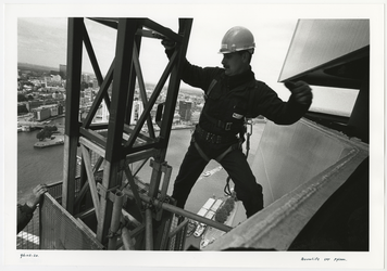 1996-2281 Een man hangt aan de bouwlift aan de top van de pyloon van de Erasmusbrug in aanbouw. Op de achtergrond is de ...