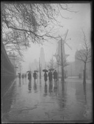 1976-4679 Wandelaars in de regen op de Coolsingel, op de achtergrond contouren van molen De Hoop.