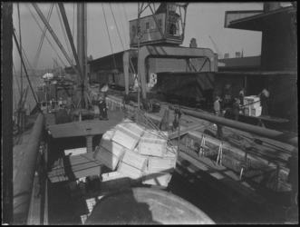 1976-5046 Laden of lossen van houten kisten van een schip aan de kade.