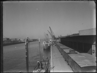 1976-5047 De Spoorweghaven. Langs de kade staan goederenwagons en een vrachtschip ligt aangemeerd langszij.