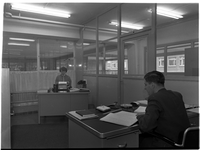 1976-7869 Een kantoor met twee personeelsleden aan bureaus. Onbekend kantoor, onbekende locatie.
