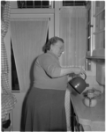 1122-2 In een keuken schenkt een mevrouw vanuit een fluitketeltje water op een filter-koffiepotje.