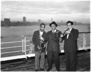 1124 Drie jazzmusici met instrumenten op dek van schip. In het midden bandleider Lionel Hampton.