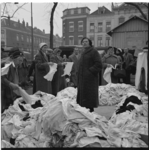 1163-1 Mensen tussen stapels kledingtextiel tijdens markt op het Noordplein.