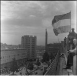 15 Vlag op Bijenkorf-in-aanbouw bij bereiken hoogste punt; HBU-gebouw en oude Bijenkorf op de achtergrond.