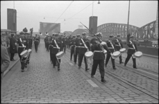20867-6-18 Tamboers en Pijpers van het Korps Mariniers marcheren door de Van der Takstraat. Rechts de spoorbrug over de ...