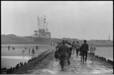 21058-2-15 Dagjesmensen wandelen op het strand en op het Noorderhoofd in een winderig Hoek van Holland. Op de ...