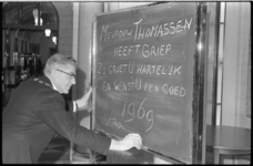 21225-1-2 Burgemeester W. Thomassen schrijft met krijt op een bord dat mevrouw Thomassen griep heeft maar iedere ...