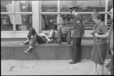 21973-7-33 Politieagent spreekt jongeren aan die voor het Centraal Station op de stenen zitbank liggen.