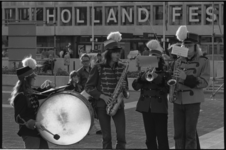 24321-2-26 Leden van een muziekkorps blazen op hun instrumenten, met de 'Holland-Festival-tekst'-gevel van de Doelen in ...