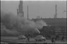 305712-6 Telefoto van kraakinstallatie en wat witte rook; op de achtergrond een woonwijk.