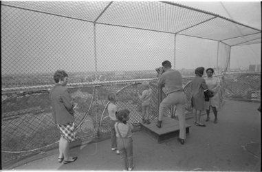 306025-9 Bezoekers op de uitkijktoren van Diergaarde Blijdorp genieten van het uitzicht door een hekwerk.