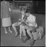 3384 Op het Centraal Station benutten twee jonge Lourdesgangers hun koffers als zitbankjes.