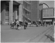 454 Mensen zitten in de zon op bankjes rond de toegangstrappen van het Beursgebouw.