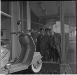 5-1 Drie mannen kijken naar scooter die in een étalage staat.