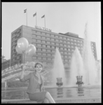 7483-2 Fotomodel 'June' poseert met Hilton-ballonnen op de rand van de waterspuitende fontein aan het Hofplein; op de ...
