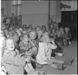 76 Kinderen zitten op de grond in een zaal; kijken naar een voorstelling.