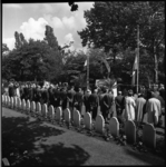 8070 Overzicht op begraafplaats Crooswijk: grafstenen, een rij mensen op de rug gefotografeerd en het monument ...