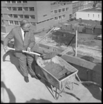 8114 D.M. Kwaak, directeur van handelsonderneming 'De Lange & Reek', schept betonmortel uit een kruiwagen en bereikt ...