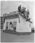 822-1 Mannen op het dak van het bestelkantoor van Gebr. van Eijsden laten de reclamepop 'Kitje Kool' naar beneden zakken.