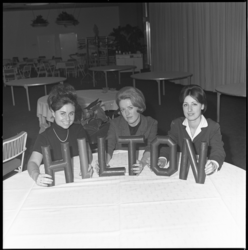 8356 Drie dames tonen de naam 'Hilton' in fysieke chocoladeletters.