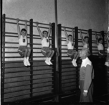 874 Een aantal jongens hangen in 'het rek' tijdens gymnastiekles door C. van Oosterom, leraar lichamelijke oefening aan ...