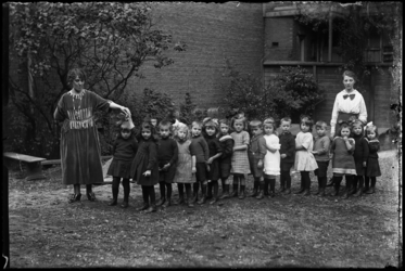 R-4918 Kleuterschool Vredenoord aan de Bethlehemstraat in Kralingen. Kinderen en leidsters staan in een rij op een ...