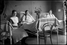 R-6538 Verpleegster zit bij twee patiënten die in bed liggen. Mogelijk in het Eudokiaziekenhuis.