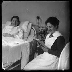 R-6540 Verpleegster leest voor uit een boek bij een patiënt in bed. Mogelijk het Eudokiaziekenhuis.