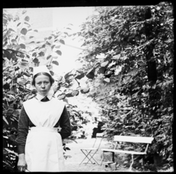 R-6561 Verpleegster poseert bij een bank in een tuin. Mogelijk bij het Eudokiaziekenhuis.