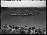 R-6684 Een fanfare omringd door kinderen loopt over het veld van Het Kasteel (Spartastadion). Op de achtergrond wordt ...